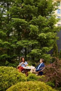 two people sitting at a table in a garden at Mona Plaza Zlatibor in Zlatibor