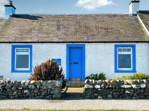 a blue door on a white house with a stone wall at Gigha in Drummore