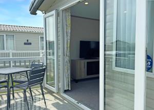 a sliding glass door leading to a patio with a table and a television at Golden Anchor Caravan Park in Chapel Saint Leonards