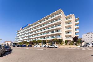 a large white building with cars parked in a parking lot at Hotel Natura Park in Comarruga