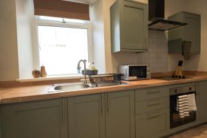 a kitchen with green cabinets and a sink and a window at Park House by Tŷ SA in Aberdare