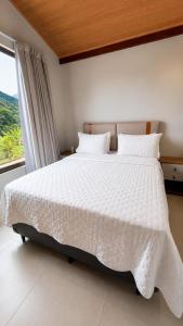 a bedroom with a white bed with a window at Chalé 1 - Vivendas do Caparaó in Pedra Menina