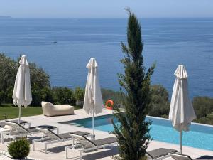 a pool with white umbrellas and chairs and the ocean at Villa Veneti in Pérdika