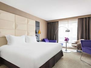 a large bed in a hotel room with purple chairs at Sofitel Warsaw Victoria in Warsaw