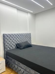 a bed in a white room with a gray padded headboard at Stan na dan in Loznica