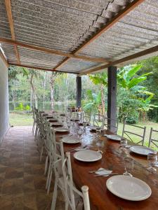 a long wooden table with white plates and chairs at Chácara Desejo do Coração 1 in Juquitiba