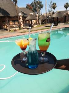 three cocktails on a tray next to a swimming pool at The Big Five Lodge in Gaborone