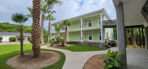 a green house with palm trees in the yard at Ground Floor, 3BR Sleeps 8, Near Ingalls and Chevron -F- in Moss Point