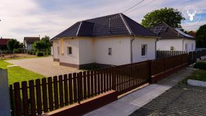 a white house with a black roof behind a fence at Rezéti vendégház in Pörböly