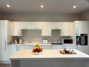 a kitchen with white cabinets and a bowl of fruit on a counter at Greenkeepers Cottage in Tobermory