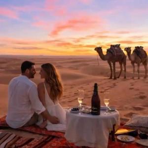 a couple sitting at a table in front of a camel caravan at Best-Merzouga traditional camps in Merzouga