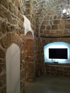 a room with a stone wall with a flat screen tv at Acre Two Wells Zimmer in ‘Akko