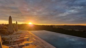 a sunset over a swimming pool with chairs and umbrellas at Podere Mantignano 2 in Faenza