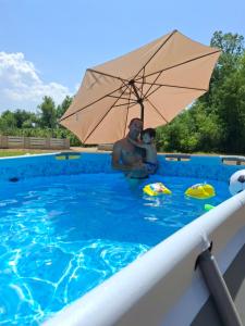 a man and a child in a swimming pool with an umbrella at Vikendica Zajecar in Zvezdan