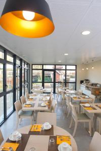 un restaurante con mesas y sillas blancas y ventanas en Logis hôtel - La Chambre D'Amiens en Amiens
