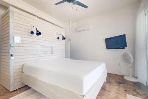 a white bedroom with a white bed and a flat screen tv at White Sands Beach House in Maya Beach