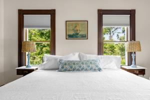a bedroom with a white bed with two windows at Inn at the Oaks in Eastham