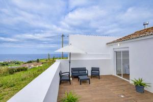 a balcony with chairs and an umbrella and the ocean at Achadinha Sunset House - São Miguel, Açores in Achadinha