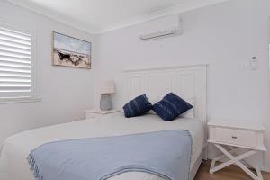 a white bedroom with a bed with blue pillows at Zilzie Beach House in Zilzie