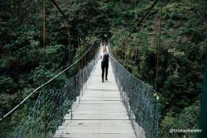 a woman walking across a suspension bridge in the forest at Colpapampa Lodge in Colcapampa