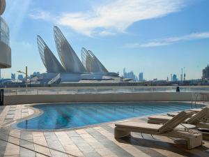 a swimming pool with two lounge chairs and a building at Saadiyat Serenity 1BR apartment with Beach access in Abu Dhabi