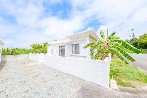 a white house with a fence and a palm tree at ふんわり in Miyakojima