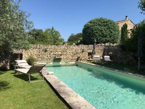 a swimming pool with chairs and a stone wall at Le Moulin des Sources in Gordes
