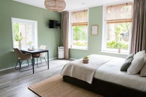 a bedroom with a bed and a table and two windows at B&B Stinzenflora - Gezellige accommodatie tussen groen en historie in Cornjum +16 photos