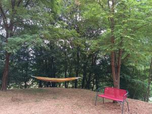 a red chair sitting next to a hammock under a tree at Le nid de bois insolite in Haget