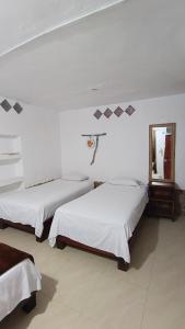 two beds in a white room with a mirror at Hostal Fragata Puerto López in Puerto López