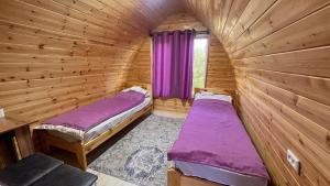 two beds in a wooden room with purple sheets at Azamat Guest House in Bokonbayevo