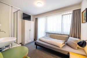 a bedroom with a bed and a sink and a window at Hotel Haus am Wald in Arosa