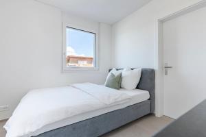 a white bedroom with a bed and a window at Rothorn Studio - Aare Jungfrau AG in Spiez