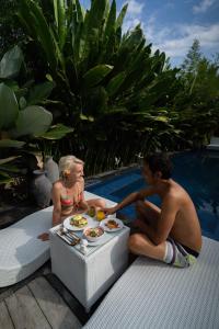 a man and a woman sitting next to a table with food at Penida Green Palm Cottage in Nusa Penida