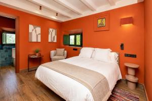 a bedroom with an orange wall with a bed and a chair at Molino de Búlar - 1920 Olive Oil Mill Heritage in Piñar +16 photos