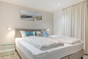 a white bedroom with a bed with white sheets at Düne in Keitum