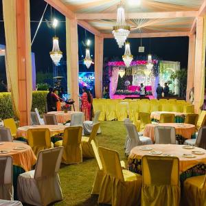 a banquet hall with yellow tables and chairs and a stage at Vani Hotel Golden Petals in Una
