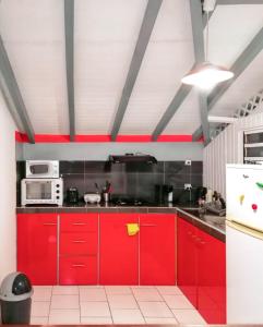 a red kitchen with red cabinets and a microwave at Appartement spacieux à Deshaies avec vue sur mer in Deshaies
