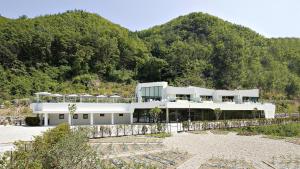 a large white building in front of a mountain at Be,Bridge Pool Villa Resort in Yeongwol
