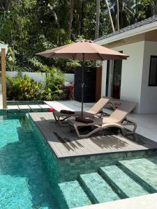 an umbrella and two chairs next to a swimming pool at Villa Manu in Ko Phangan