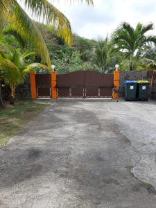 a gate in a driveway with trash cans and palm trees at Studio charmant à Le Robert - 17 m² avec Piscine partagée in Le Robert