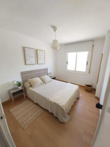 a white bedroom with a bed and a large window at Charming apartment with mountain view in Francàs - 45m² in Comarruga