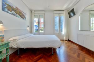 a bedroom with a bed with white sheets and wood floors at Hostal Costa Coruña in A Coruña
