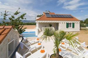 a group of white chairs and a house with solar panels at Charming Villa in Pučišća + Pool in Pučišća