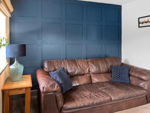 a brown leather couch in a living room with a blue wall at Old Master's Cottage in Leven
