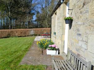 a building with a bench and flowers in a yard at Keepers Cottage Burradon in Sharperton