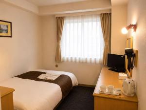 a hotel room with a bed and a desk with a television at Saga Idaimae Green Hotel in Saga