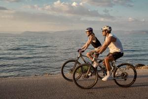 two people riding bikes on a beach near the water at Mythos Palace Resort - Adults Only in Boukari