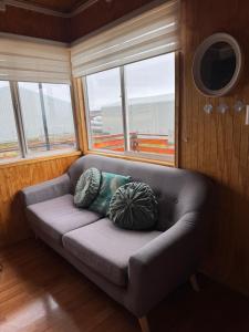 a couch with two pillows sitting in a room with windows at Depto huerto 23 in Puerto Natales