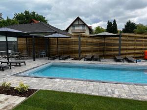 a swimming pool with chairs and umbrellas and a house at Best Apartman Lelle 2 in Balatonlelle